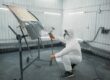 A technician spray-painting the bonnet of a car inside a booth.