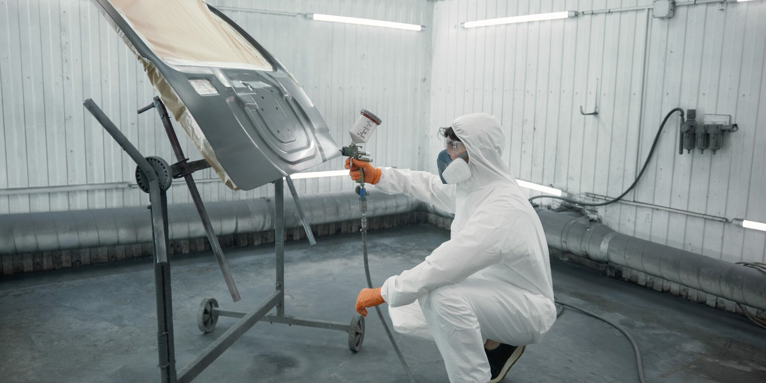 A technician spray-painting the bonnet of a car inside a booth.