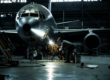 Technician welding metal on an airplane nose inside a maintenance hangar.