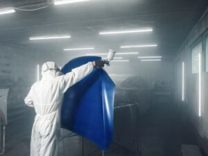 automotive Worker spray painting a blue automotive part in a paint booth.